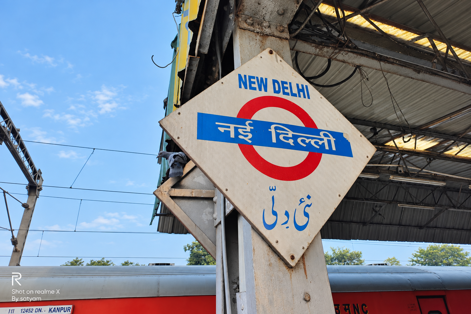 AI-modified archive editorial image of the New Delhi station sign photographed by Satyamatic in 2019; not today’s service restoration.